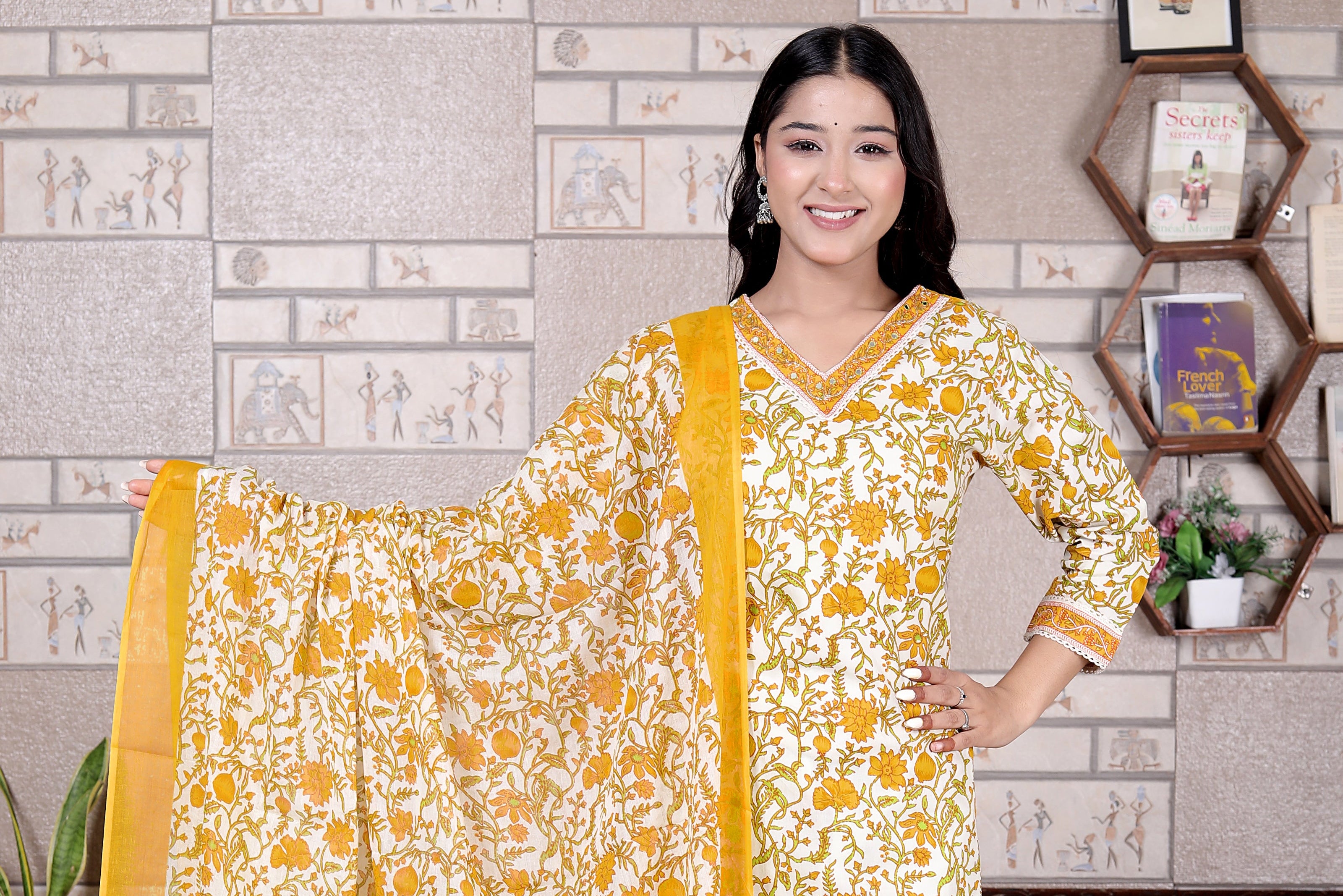 Woman wearing a yellow and white traditional outfit with a floral pattern in a room.